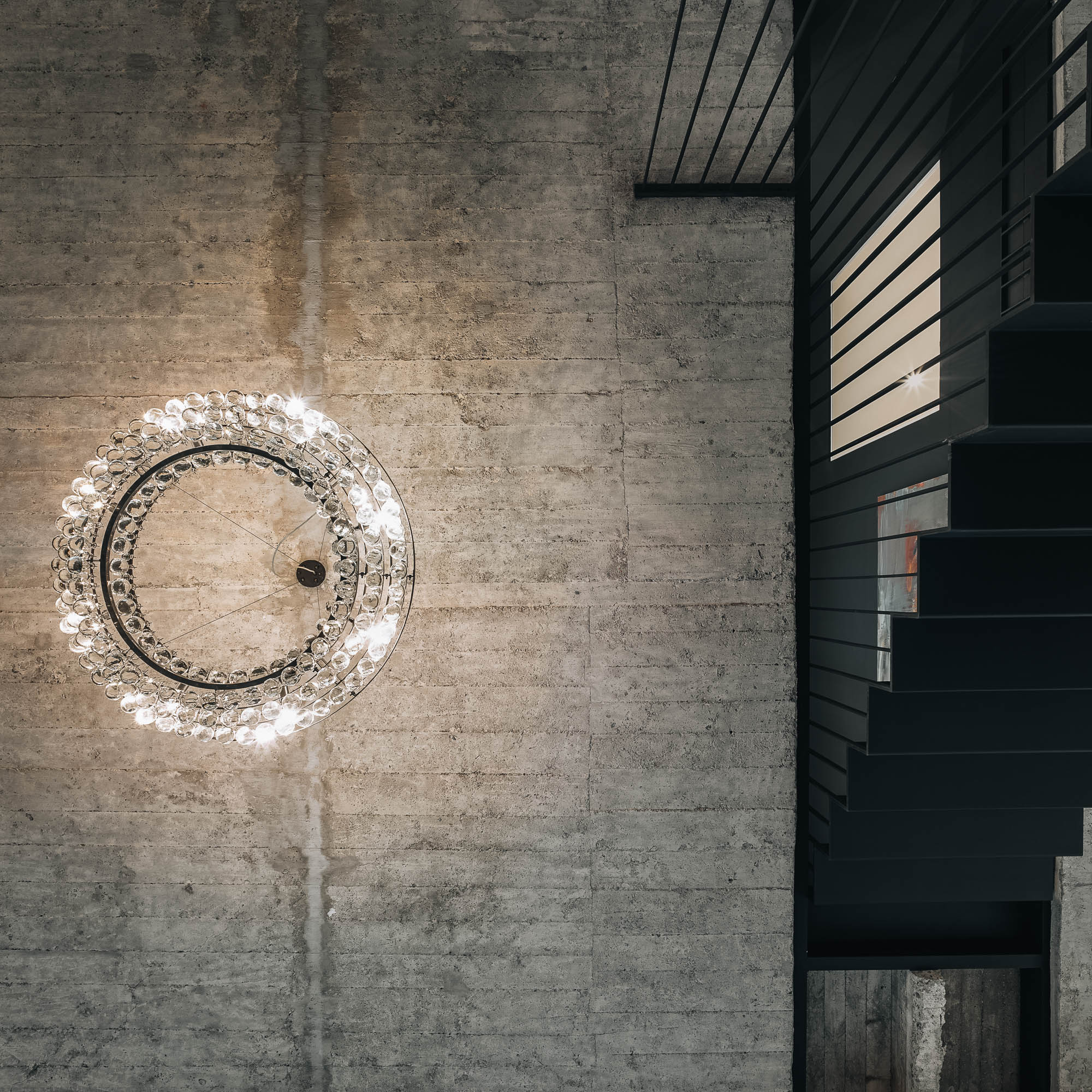 Crystal ring chandelier detail against raw exposed concrete ceiling black steel staircase structure OOOOX