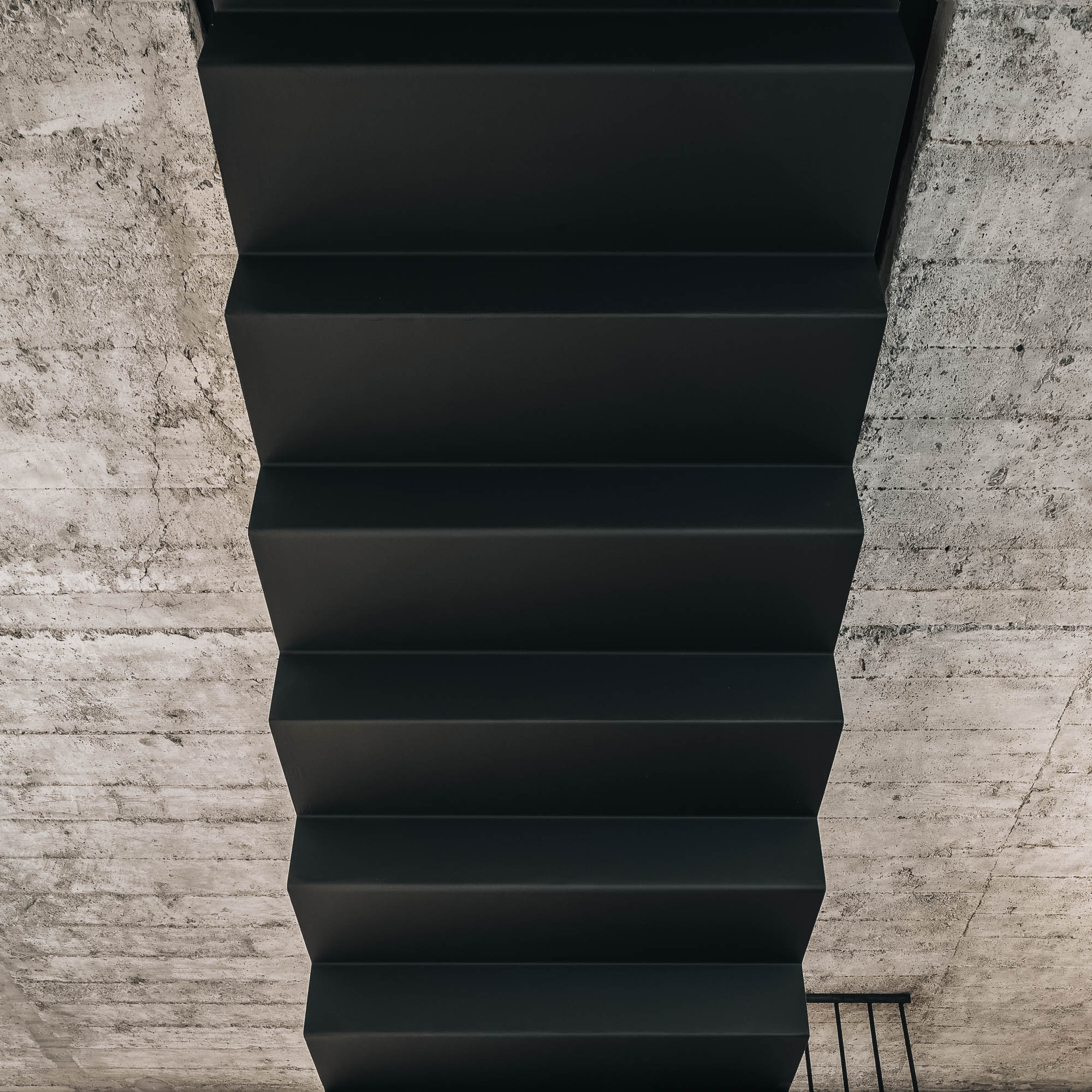 Black steel floating staircase viewed from below raw exposed concrete slab walls abstract composition OOOOX