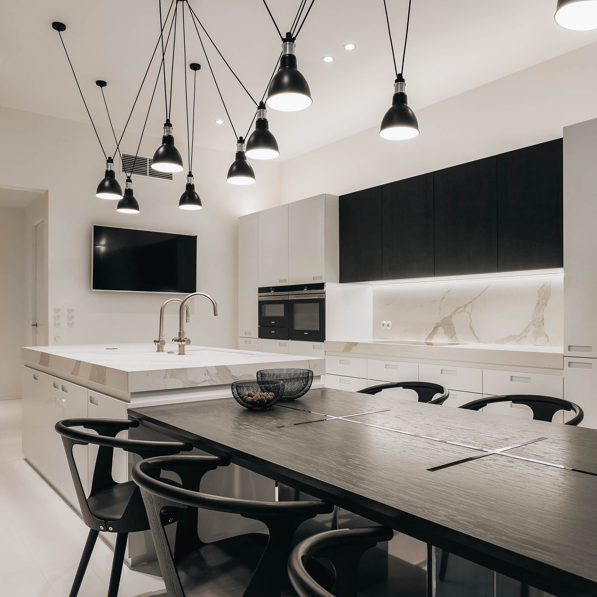 Dining table dark oval top black round-back chairs white marble island kitchen appliances spider pendants OOOOX